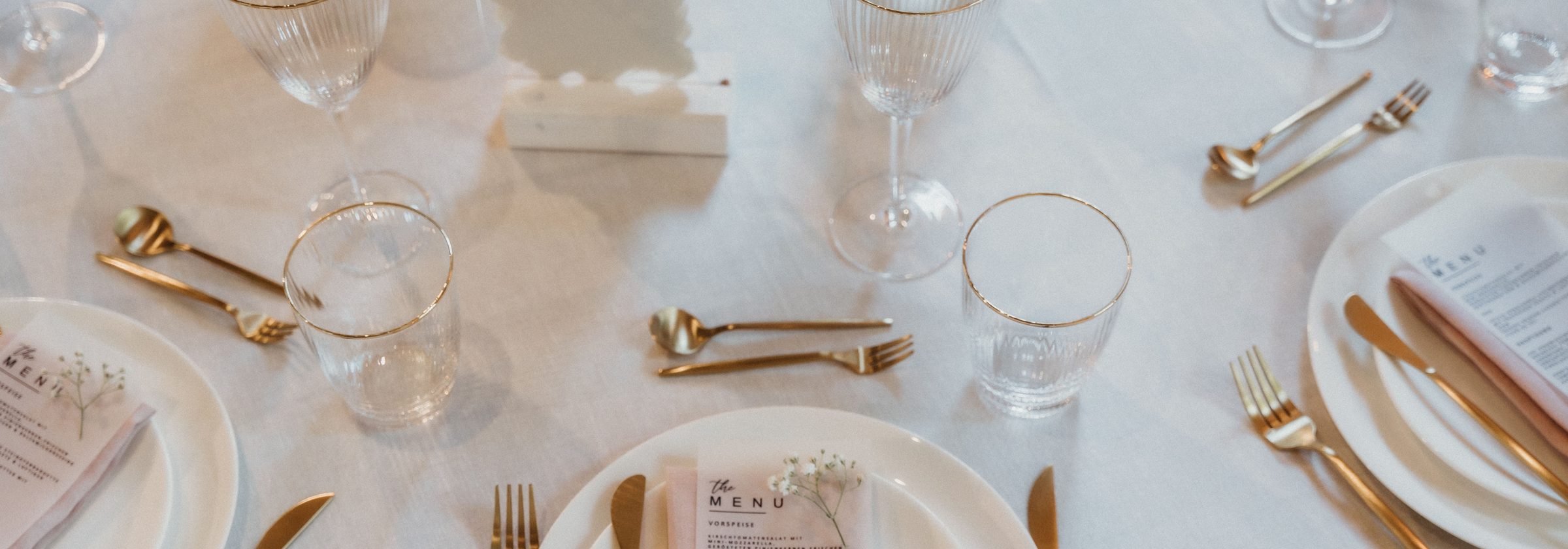 Table dressée : assiettes blanches à liseré, couverts dorés et verres à filet or